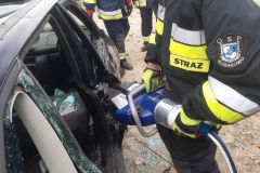 Strażak OSP za pomocą narzędzi technicznych próbuje dostać się do uszkodzonego pojazdu