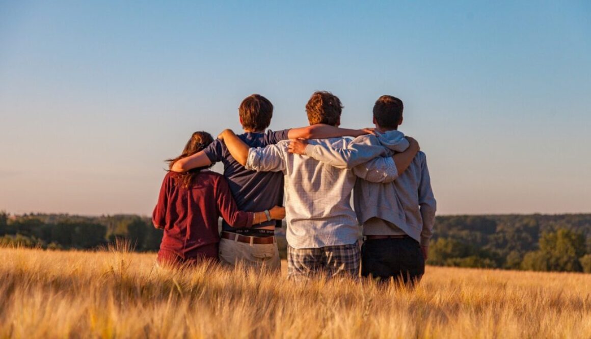 Grupa młodych ludzi na polu zboża trzyma się za ramiona