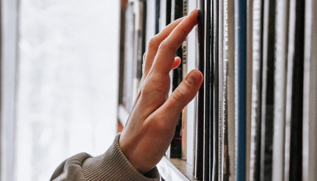 Zbliżenie na rękę nastolatka, szukającego odpowiedniej książki na półce