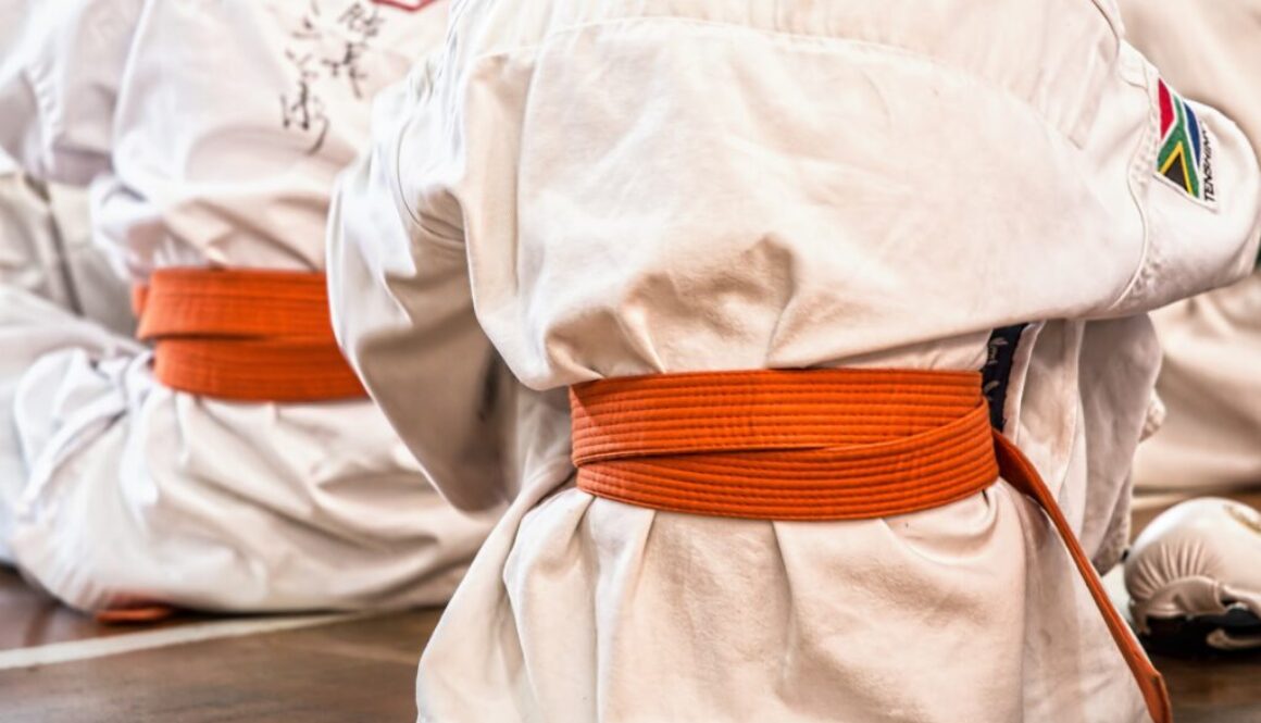 Zawodnicy karate siedzący po turecku w pomarańczowych pasach