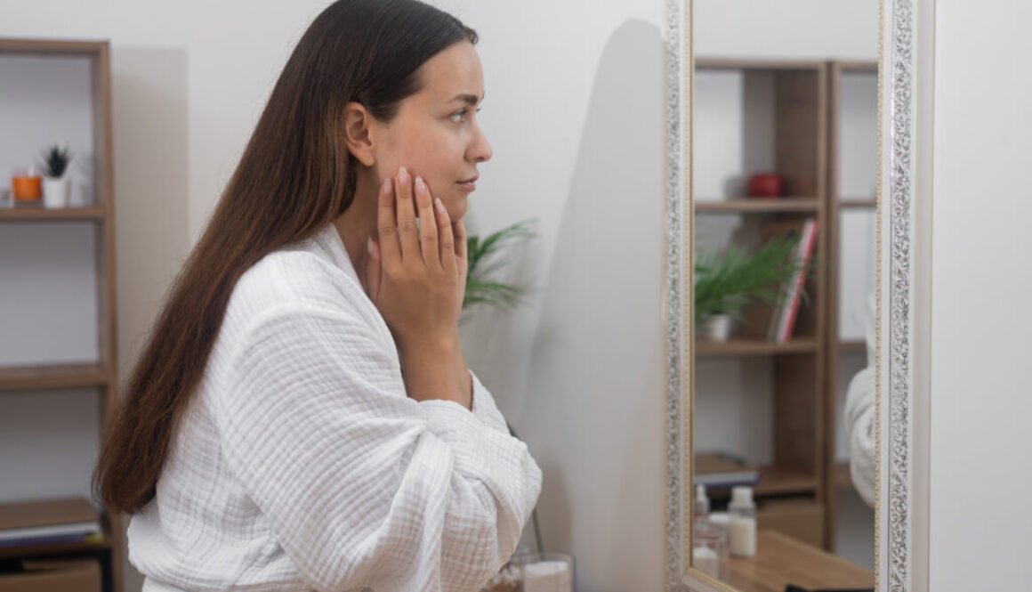 Home skincare: woman in a bathrobe examines her reflection in the bathroom mirror
